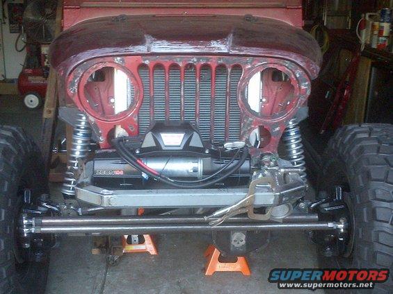 1985 Jeep CJ7 front end undergoing modification, showing grille, headlights removed, and a winch installed