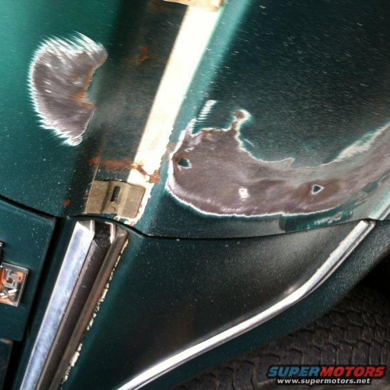 Green car body panel with exposed metal, rust, and primer patches, showing damage and repair work