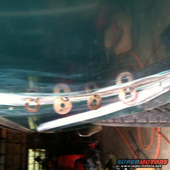 Close-up of metal mounting rings attached to a curved green panel, possibly from a vehicle's undercarriage