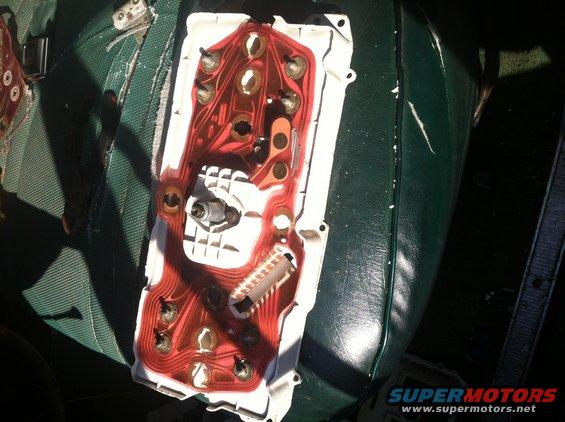 back of car dashboard gauge cluster with red circuit board and metal contacts