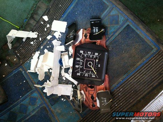 Broken dashboard trim pieces scattered around a speedometer and fuel gauge