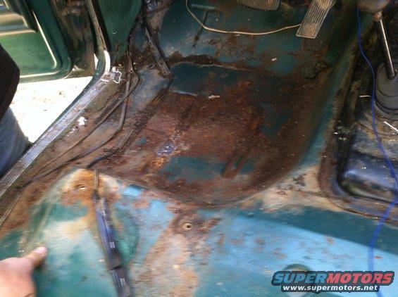 Rusty teal interior floor of a vehicle with visible wiring and pedals