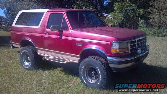 1995 Ford Bronco parked on grass, red body with white removable top