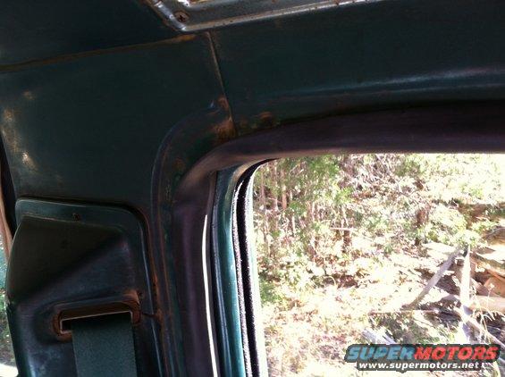 Green interior of a vehicle with a seatbelt visible and a roll bar above the window