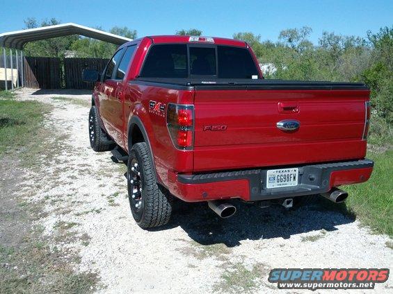 Red 2010 Ford F-150 pickup truck, rear 3/4 view, with aftermarket wheels and tinted taillights