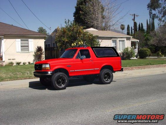 Red Ford Bronco parked on street, lifted with off-road tires and roof lights