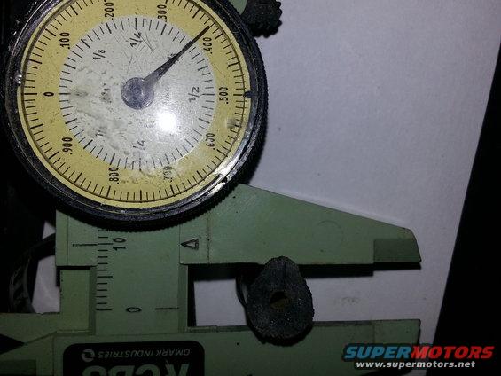 Dial indicator and caliper measuring a small, dark, circular part with a hole in the center