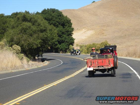 Red 1946 Jeep CJ5 driving on a road with another vintage car behind it