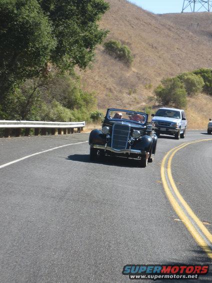 dark blue convertible driving on a road with a white pickup truck behind it