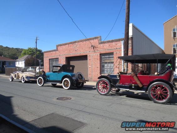 Three antique cars parked on a street, two convertibles and one touring car