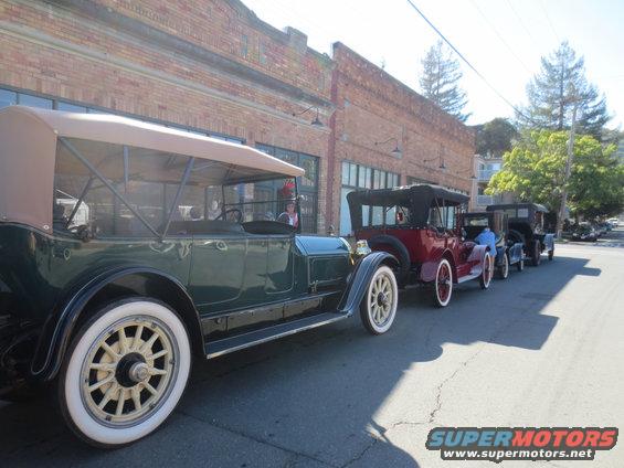 Green touring car with a tan top and white-walled tires parked in a line with other vintage cars