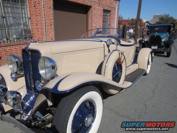 Tan convertible with blue trim and side-mounted spare tire, parked behind a blue vintage car