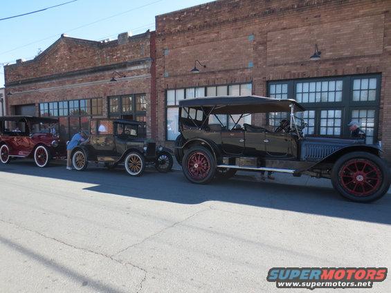 three old touring cars parked in front of a brick building