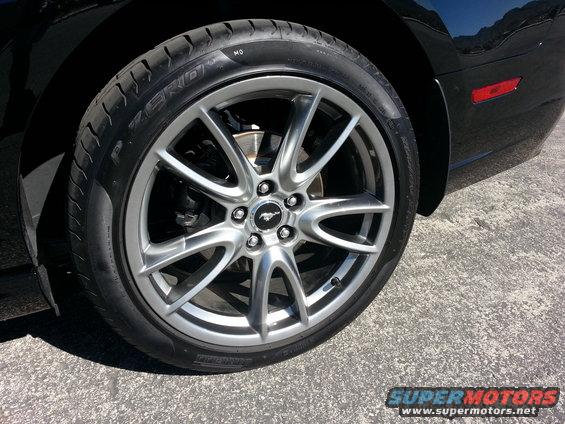 Close-up of a 2013 Ford Mustang's silver five-spoke wheel and tire. The car is black