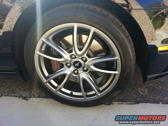 Black car's front wheel with silver five-spoke rims and red brake calipers. Tire has 'OUTSIDE' text