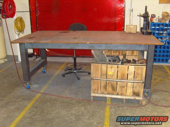 Workbench with metal top, wooden crates for storage underneath, and a rolling stool. Red curtain in background