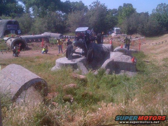 Off-road buggy on rocks, with other vehicles and obstacles in background