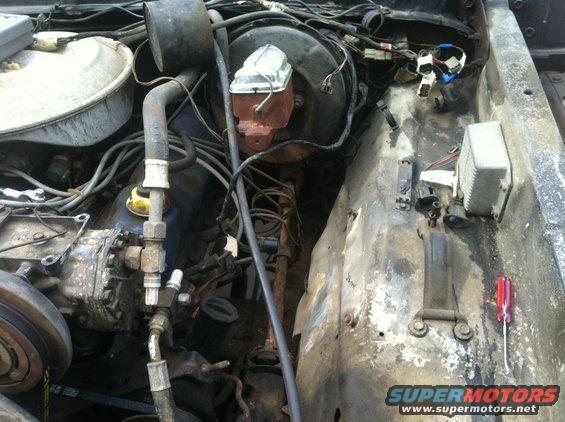 Engine bay showing brake booster, master cylinder, and various hoses and wires. A screwdriver rests on the fender