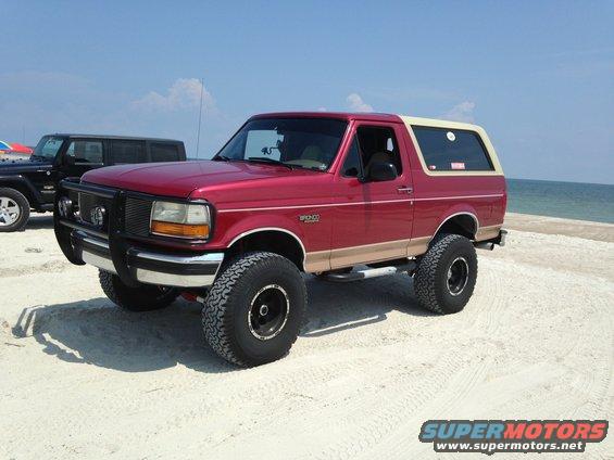 Red and tan 1994 Ford Bronco with aftermarket bumper and large tires on a sandy beach