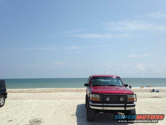 Red SUV with a bull bar parked on a sandy beach with the ocean in the background