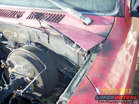 Close-up of a damaged vehicle engine bay with a red hood and a brake booster