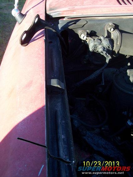 Black metal bracket attached to red vehicle fender, with engine components visible behind