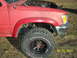 1991 Toyota Pickup/SR5 - Front quarter view of a red 1991 Toyota Pickup SR5 with a large off-road tire and exposed engine components.