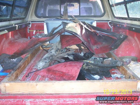 Pile of red car body parts in a truck bed with a camper shell