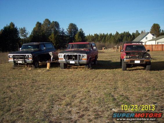 Three trucks parked in a grassy field under a clear blue sky