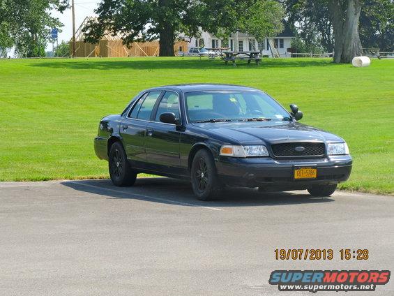 Black 2003 Ford Crown Victoria sedan parked on asphalt, front-left view, with a yellow license plate