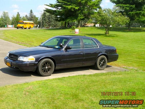 Dark blue 2003 Ford Crown Victoria sedan parked on a concrete driveway, black wheels, slight damage on front bumper