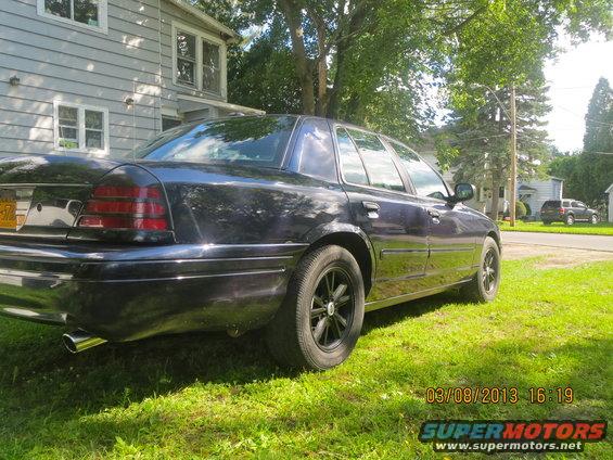 Dark sedan parked on grass in front of a house. Another SUV is visible in the background