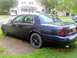 2003 Ford Crown Victoria - A dark blue 2003 Ford Crown Victoria is parked on a grassy area next to a driveway.