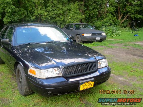 Front view of a dark blue 2003 Ford Crown Victoria with a black grille, parked next to another Ford Crown Victoria