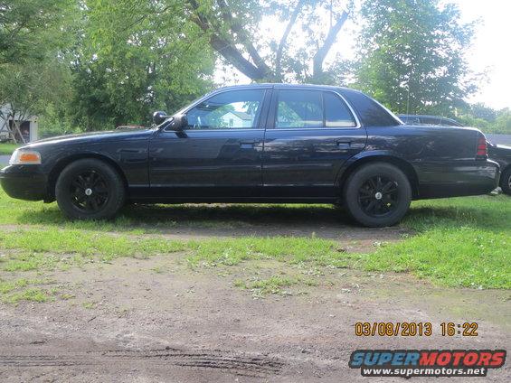 Dark blue 2003 Ford Crown Victoria sedan, side view, black wheels, parked on grass