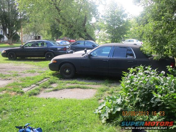 Side view of a black 2003 Ford Crown Victoria with tinted windows and a police spotlight