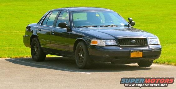 Black 2003 Ford Crown Victoria parked on asphalt with a grassy field behind it