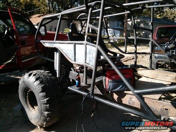 Red off-road vehicle with extensive roll cage, large tires, and a cooler. Another vehicle is partially visible to the right