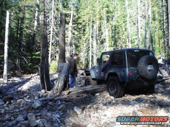 Dark blue 2005 Jeep Wrangler on a rocky trail with two people standing nearby
