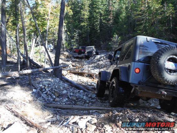 2005 Jeep Wrangler on a rocky, wooded trail with other Jeeps behind it