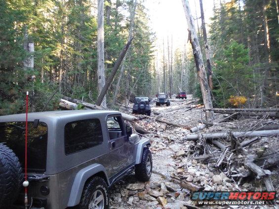 Gray Jeep Wrangler on a rocky forest road with other Jeeps behind