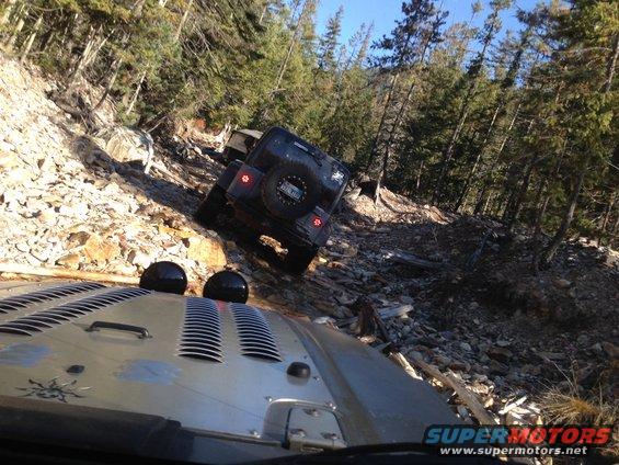 Two Jeep Wranglers driving up a steep, rocky mountain trail with trees on either side