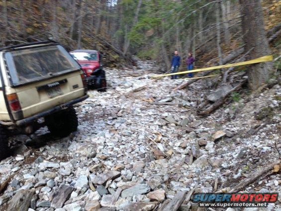 Tan Toyota pickup truck and red Jeep Wrangler on a rocky trail. Toyota badge visible