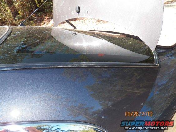 Dark gray car rear window seal with hood open. Watermarks and dust visible on the seal