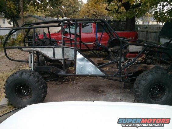 Custom off-road buggy frame with large tires, red pickup truck in background