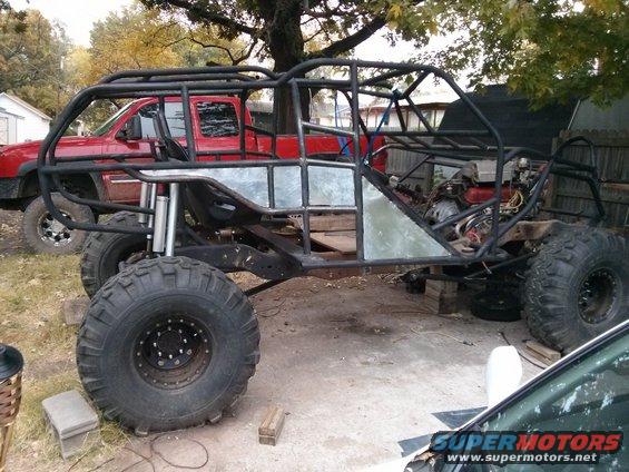 Custom buggy with roll cage and large tires, red pickup truck in background