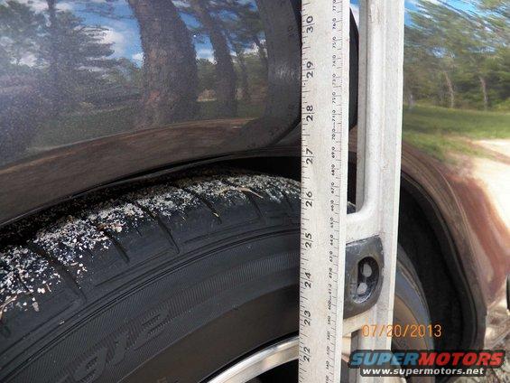 Dark gray car tire and fender with sand, ruler measuring ride height