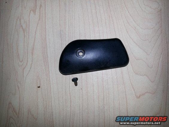 Black plastic trim piece with screw hole and a separate screw on a wooden surface