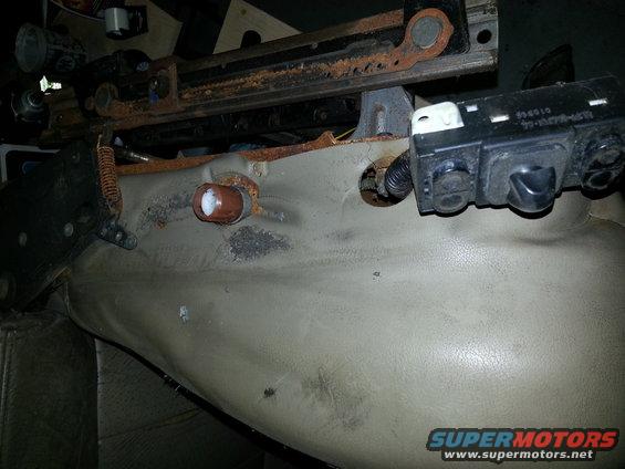 Close-up of a car seat's metal frame, beige upholstery, and a black electronic control module with visible text