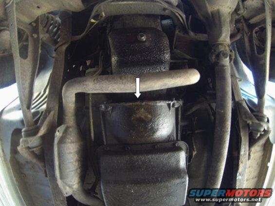 Underside view of vehicle showing exhaust pipe, catalytic converter, and oil pan. Arrow points to oil pan